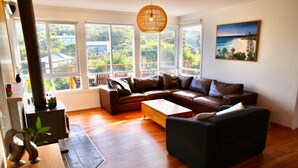 A living room with a brown leather sofa, a black armchair, a wooden coffee table, and a large window with a view of greenery and buildings.