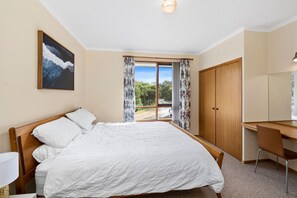 A bedroom with a bed, a desk, a wardrobe, and a window with curtains.