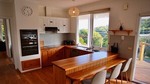 A modern kitchen with wooden cabinets, a built-in oven, a large island with bar stools, and a window providing a view of the outdoors.