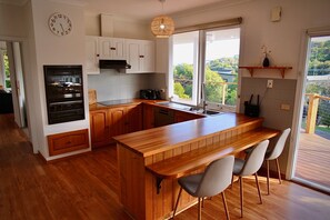 Eine moderne Küche mit Holzschränken, einem Einbauofen, einer großen Kücheninsel mit Barhocker und einem Fenster mit Blick ins Freie.