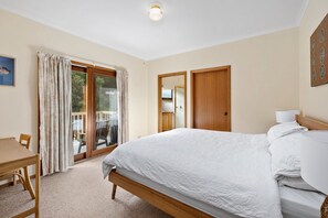 A bedroom with a bed, a desk, a chair, a sliding glass door, and a mirror. - Cowallinga (Fairhaven)