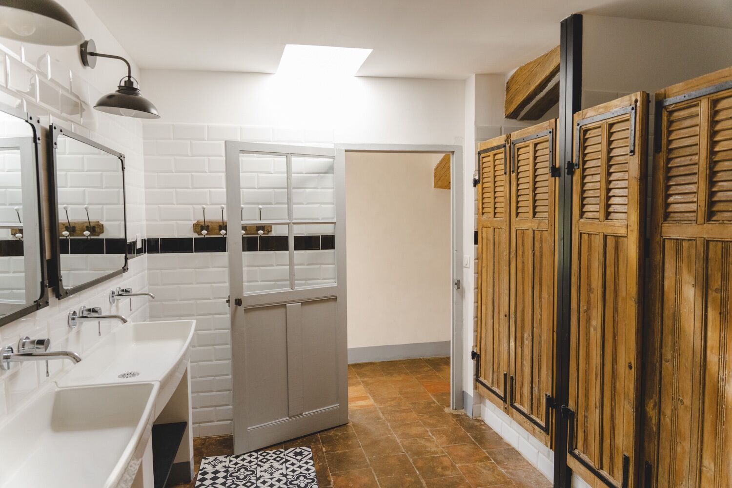 A bathroom with white tiled walls, a white sink, a mirror, and a wooden door.