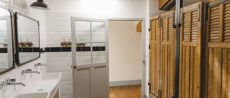 A bathroom with white tiled walls, a white sink, a mirror, and a wooden door.