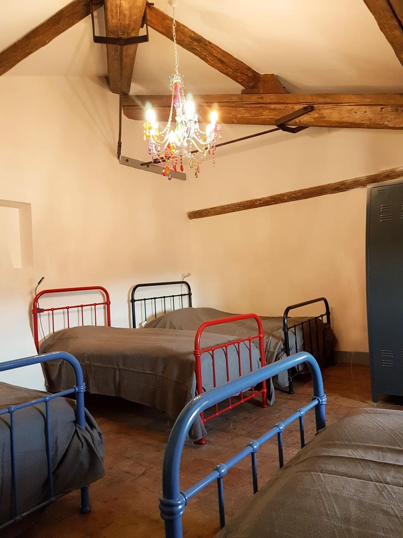 Une chambre de dortoir avec trois lits superposés en métal, un plafond en bois et un lustre.