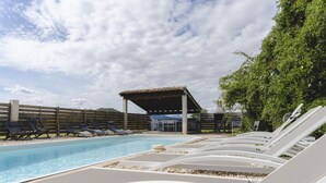 Une piscine avec des chaises longues, un espace salon couvert et une vue sur une montagne en arrière-plan.