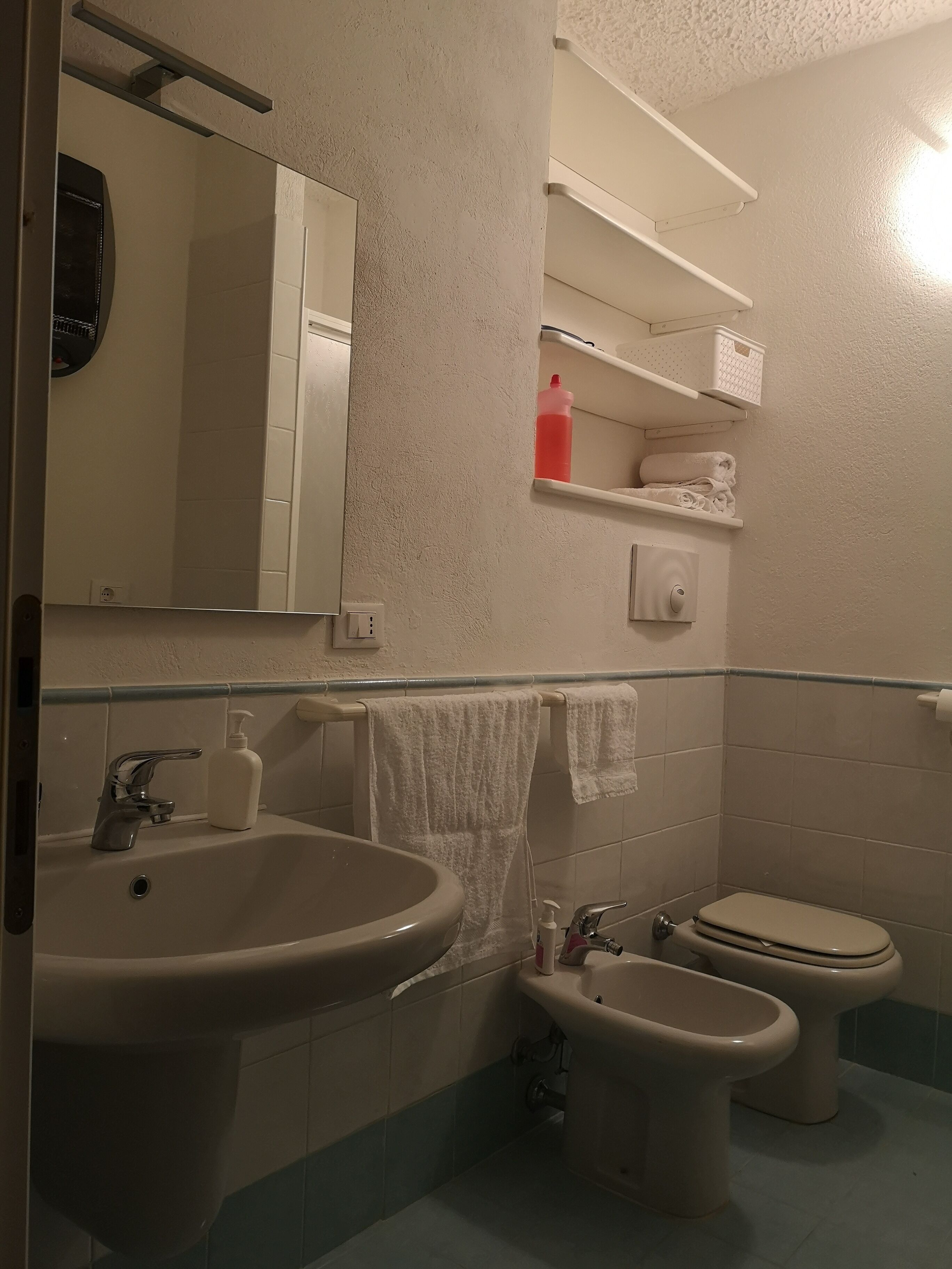 Een badkamer met een wastafel, bidet, toilet en planken met toiletartikelen.