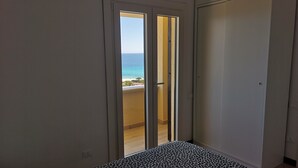 A room with a bed, a wardrobe, and a door leading to a balcony with a view of the sea. - SWEET HOME CAMILLA Costa Rei with Panoramic Terrace 300 meters from the beach (Costa Rei)