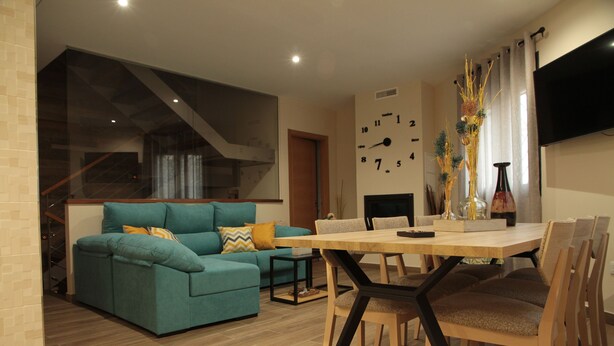 Un salon moderne avec un canapé de couleur turquoise, une table à manger en bois et des chaises. On y trouve une cheminée avec une horloge au mur, et un téléviseur fixé au-dessus.
