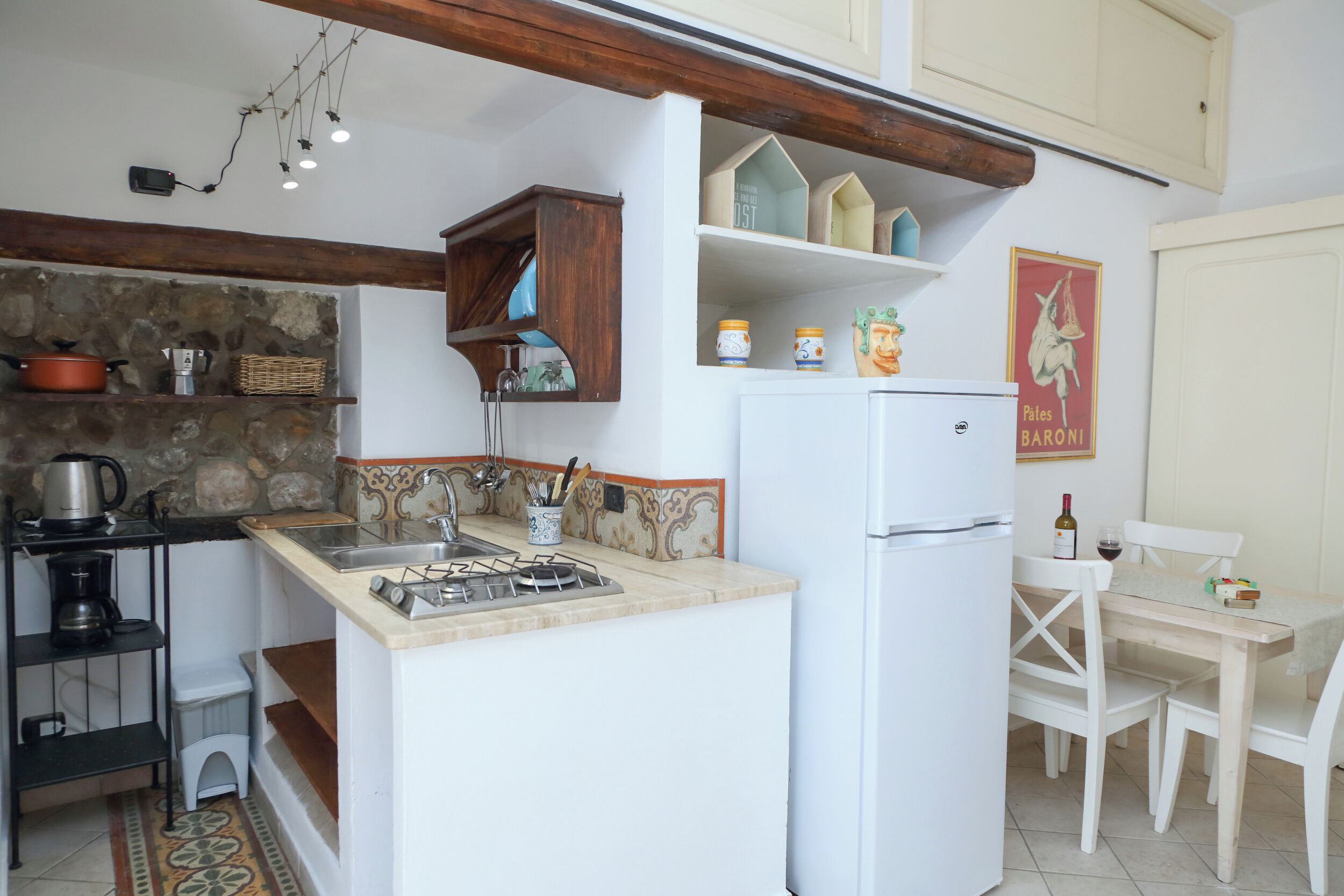 Una cucina compatta con piano cottura a gas, frigorifero bianco e un piccolo angolo ristoro con tavolo e sedie bianche.