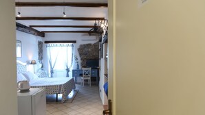 A bedroom with a bed, desk, and chair, a stone wall, and a kitchenette area. - Room with balcony and beautiful sea view in the old town (Cefalù)
