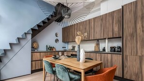 A modern kitchen with a wooden cabinet, a dining table with chairs, and a staircase with a unique light fixture.