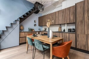 A modern kitchen with a wooden cabinet, a dining table with chairs, and a staircase with a unique light fixture.