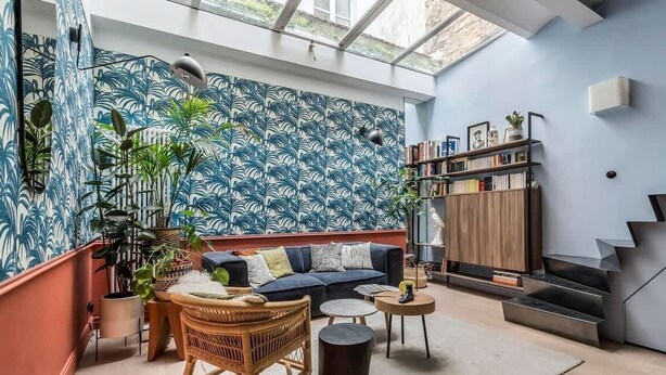 A modern living room with a blue patterned wall, a sofa, a coffee table, and a bookshelf.