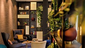 A modern lounge area with leather chairs, a small round table, and a bookshelf with various decorative items and plants. - Motel One Aachen (Aachen)