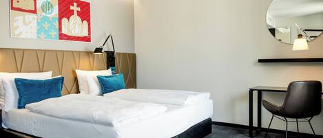 A hotel room with a bed, pillows, a desk, a chair, and wall art.