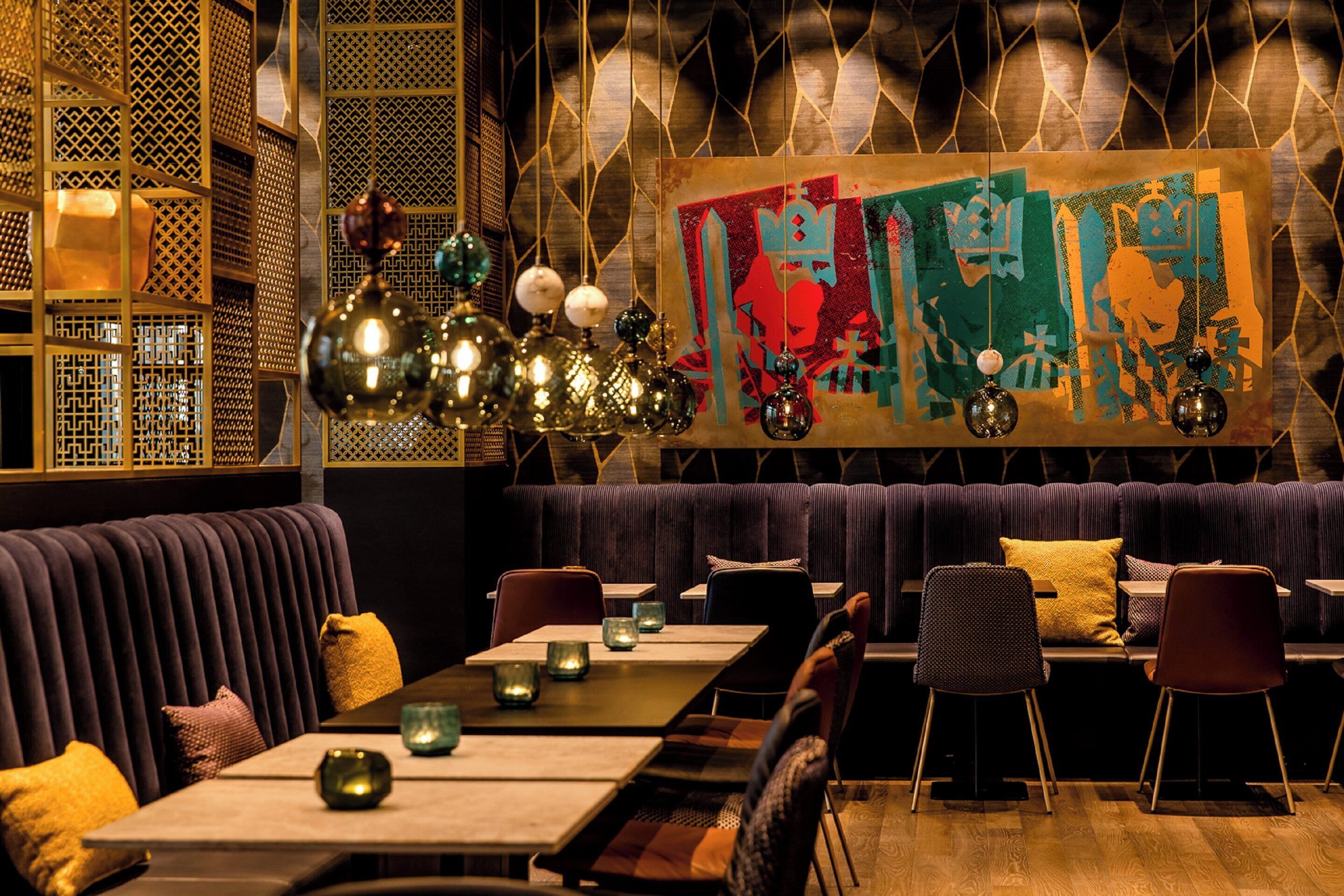 A restaurant with a long table, cushioned seating, and hanging decorative lights.