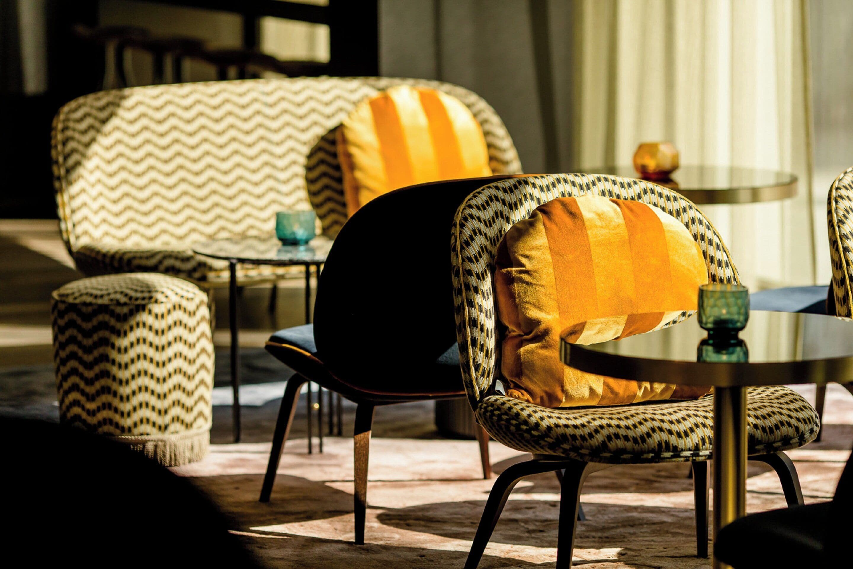 Uma área de estar acolhedora com cadeiras e pufes estampados, uma mesa redonda e um vaso decorativo.