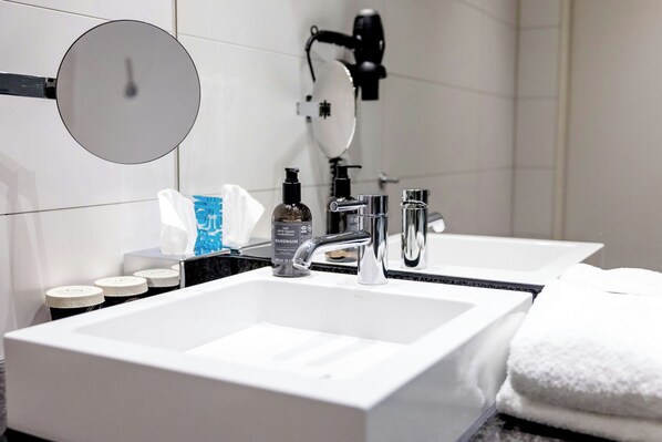 Un baño moderno con un lavamanos blanco grande, un espejo y un cabezal de ducha manual.