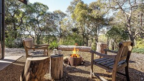 An outdoor seating area with wooden benches and a central fire pit. - Nestled amongst the leafy trees, Gum Nuts a very Australian styled simple but sophisticated property (Yallingup)