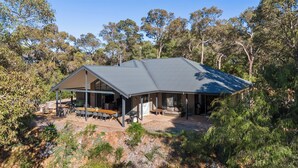 A modern house with a covered patio, outdoor seating, and a large window overlooking a forested area. - Gum Nuts - Nestled amongst the leafy trees, Australian styled simple & relaxing (Yallingup)