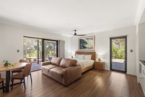 A modern bedroom with a bed, a sofa, a dining table, and a ceiling fan. - Gum Nuts - Nestled amongst the leafy trees, Australian styled simple & relaxing (Yallingup)