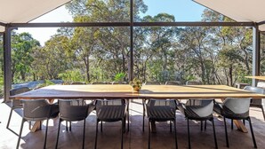 A large table with six chairs, a potted plant, and a view of trees through a large window. - Gum Nuts - Nestled amongst the leafy trees, Australian styled simple & relaxing (Yallingup)