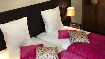 Cama bem arrumada com roupa de cama branca e rosa, cabeceira e abajur.