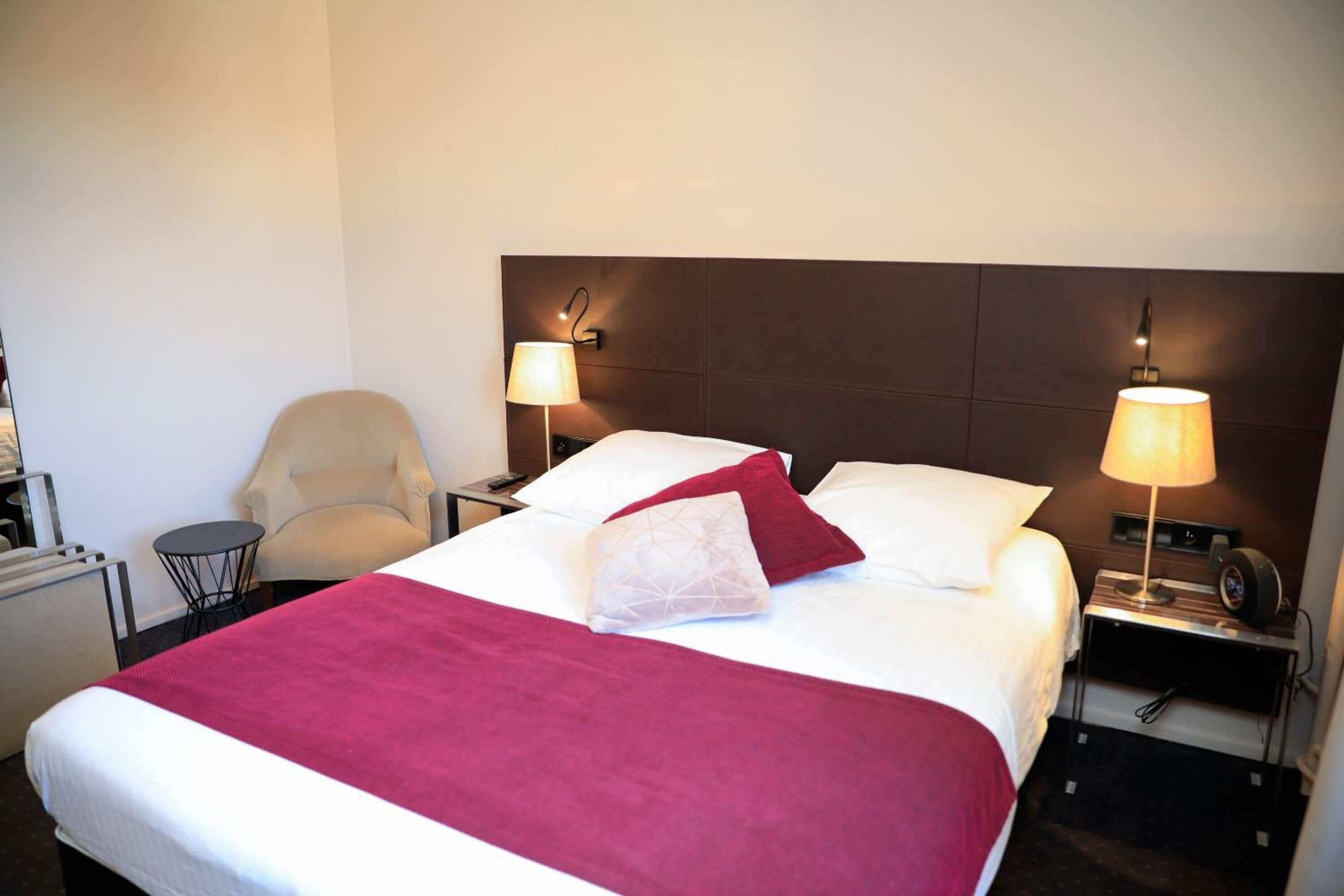Quarto de hotel com uma cama grande, duas mesas de cabeceira com luminárias, uma cadeira e uma pequena mesa.