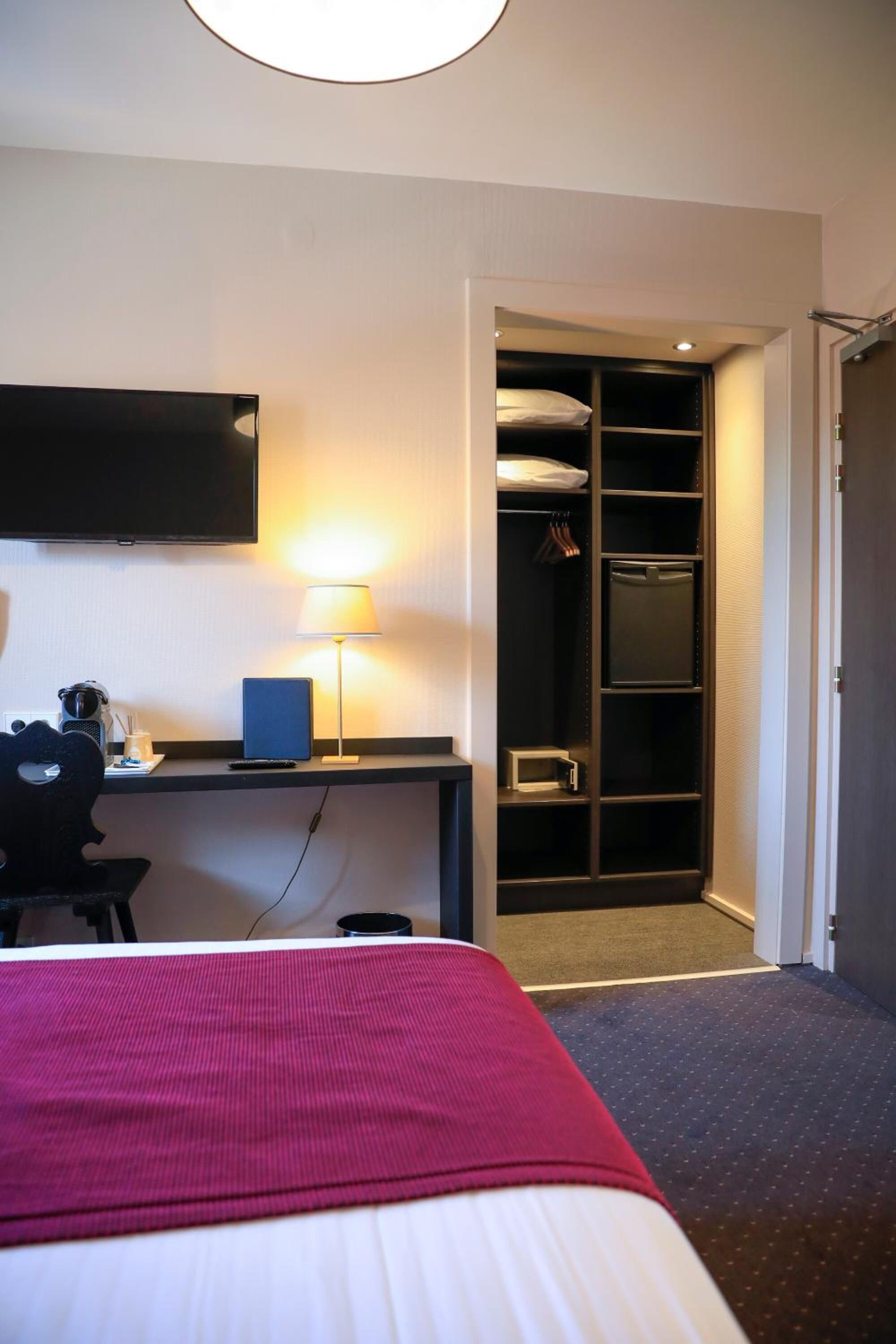 Habitación de hotel con cama, escritorio, lámpara, televisión y vestidor.