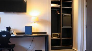 Habitación de hotel con cama, escritorio, lámpara, televisión y vestidor.