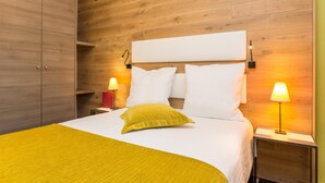 Ein Hotelzimmer mit einem hölzernen Kopfteil, einem Bett mit weißen Laken und einer gelben Tagesdecke sowie zwei Nachttischlampen.