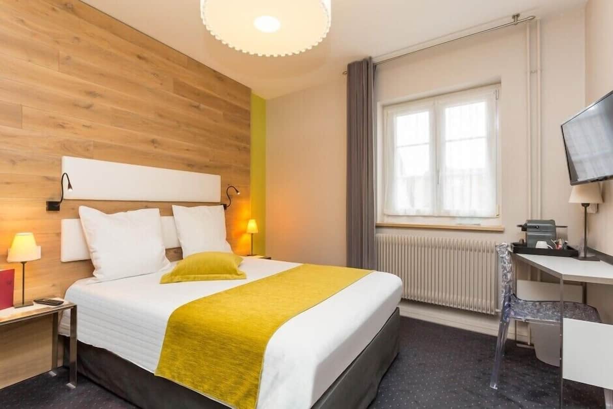 A hotel room with a bed, a desk, a chair, a TV, and a window.