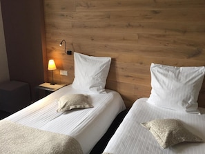Two single beds with white linens and pillows, a nightstand with a lamp, and a wooden headboard. - Auberge Alsacienne (Eguisheim)