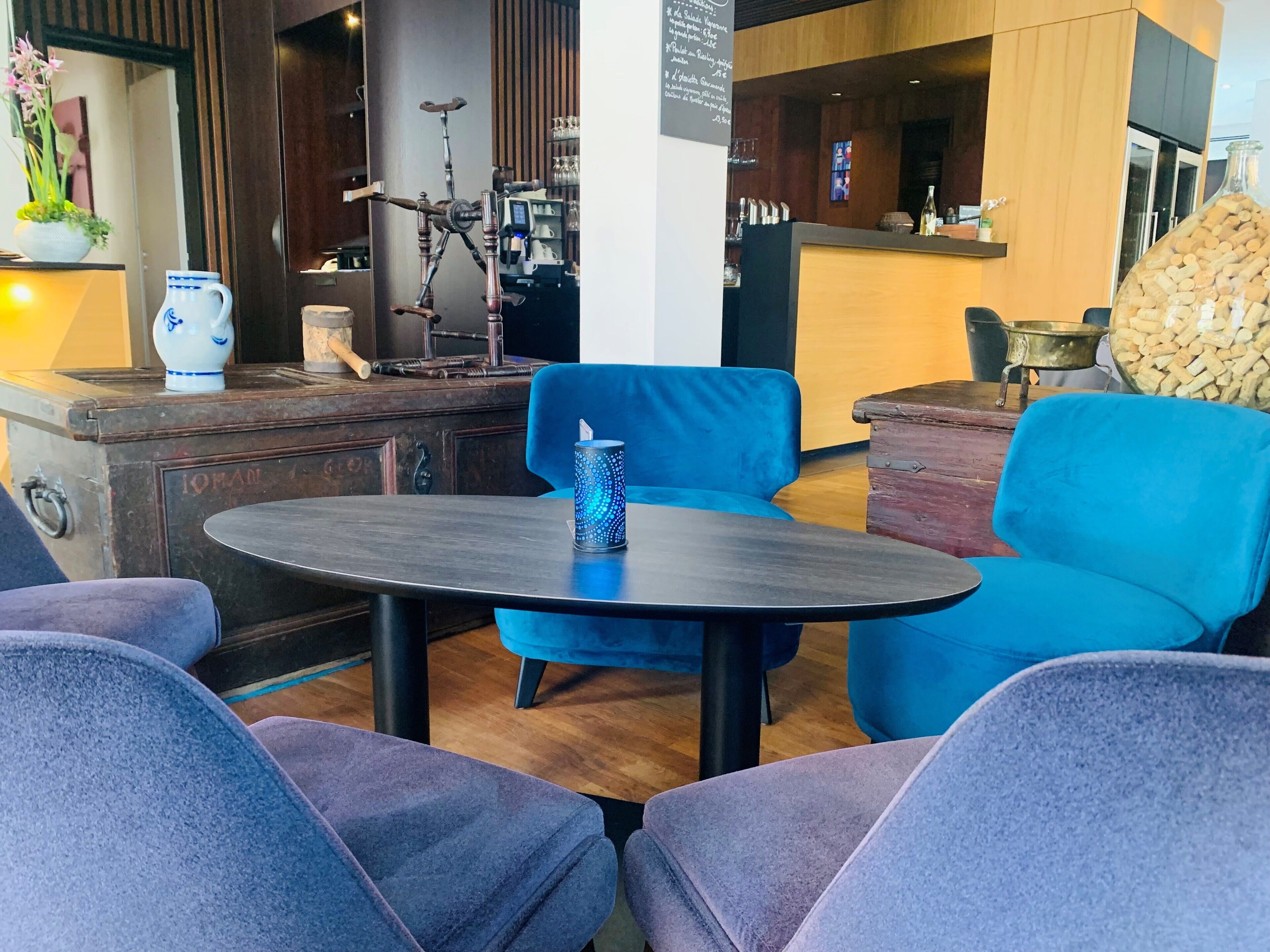 Un espacio lounge moderno con una mesa redonda, sillas azules, un jarrón decorativo y un mueble de madera.