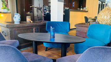 Un espacio lounge moderno con una mesa redonda, sillas azules, un jarrón decorativo y un mueble de madera.