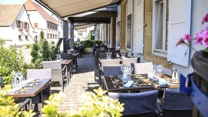 Ein Straßencafé mit Tischen und Stühlen, einem überdachten Gang und Gebäuden im Hintergrund.