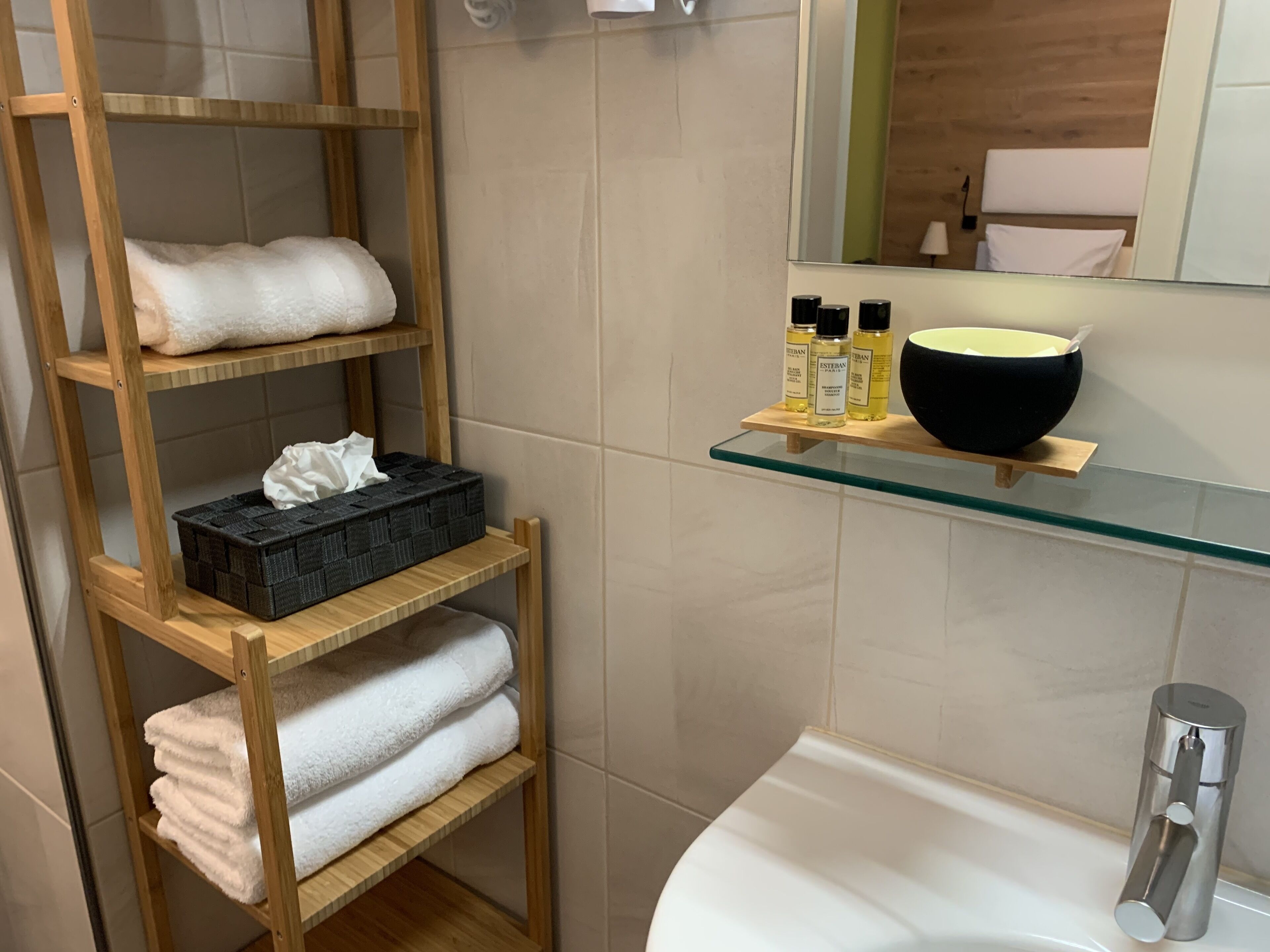 Ein Badezimmer mit einer Holzwandregal, auf der Handtücher und Toilettenartikel stehen, einem schwarzen Waschbecken auf einer Glasablage und einem modernen Waschplatz.