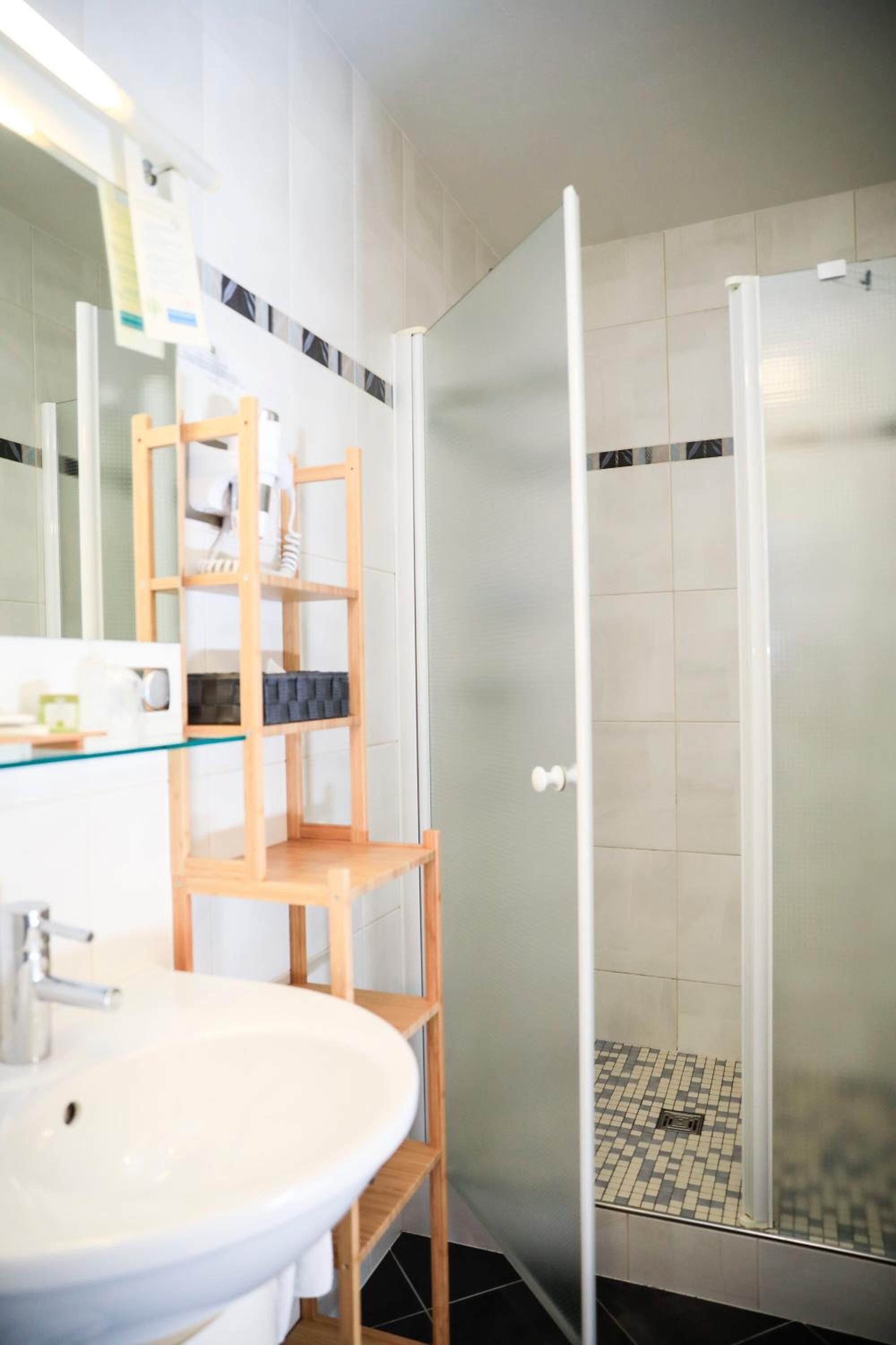 A bathroom with a glass shower enclosure, a wooden shelf unit, and a white sink.
