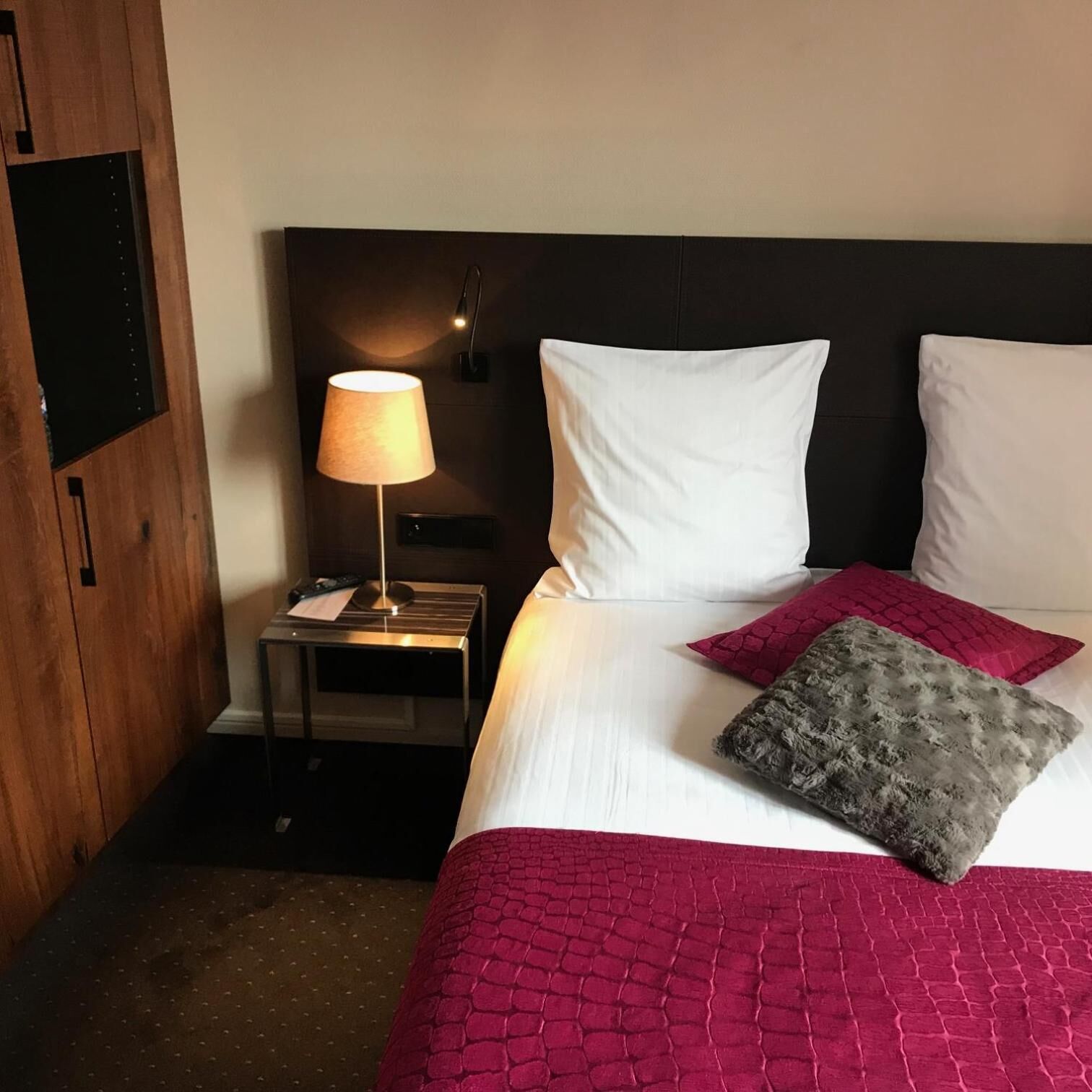 A hotel room with a bed, a nightstand, a lamp, and a television.