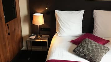 A hotel room with a bed, a nightstand, a lamp, and a television.