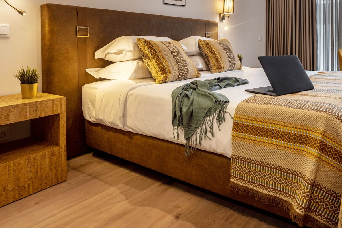 A bedroom with a bed, a laptop, a bedside table with a plant, and a headboard.