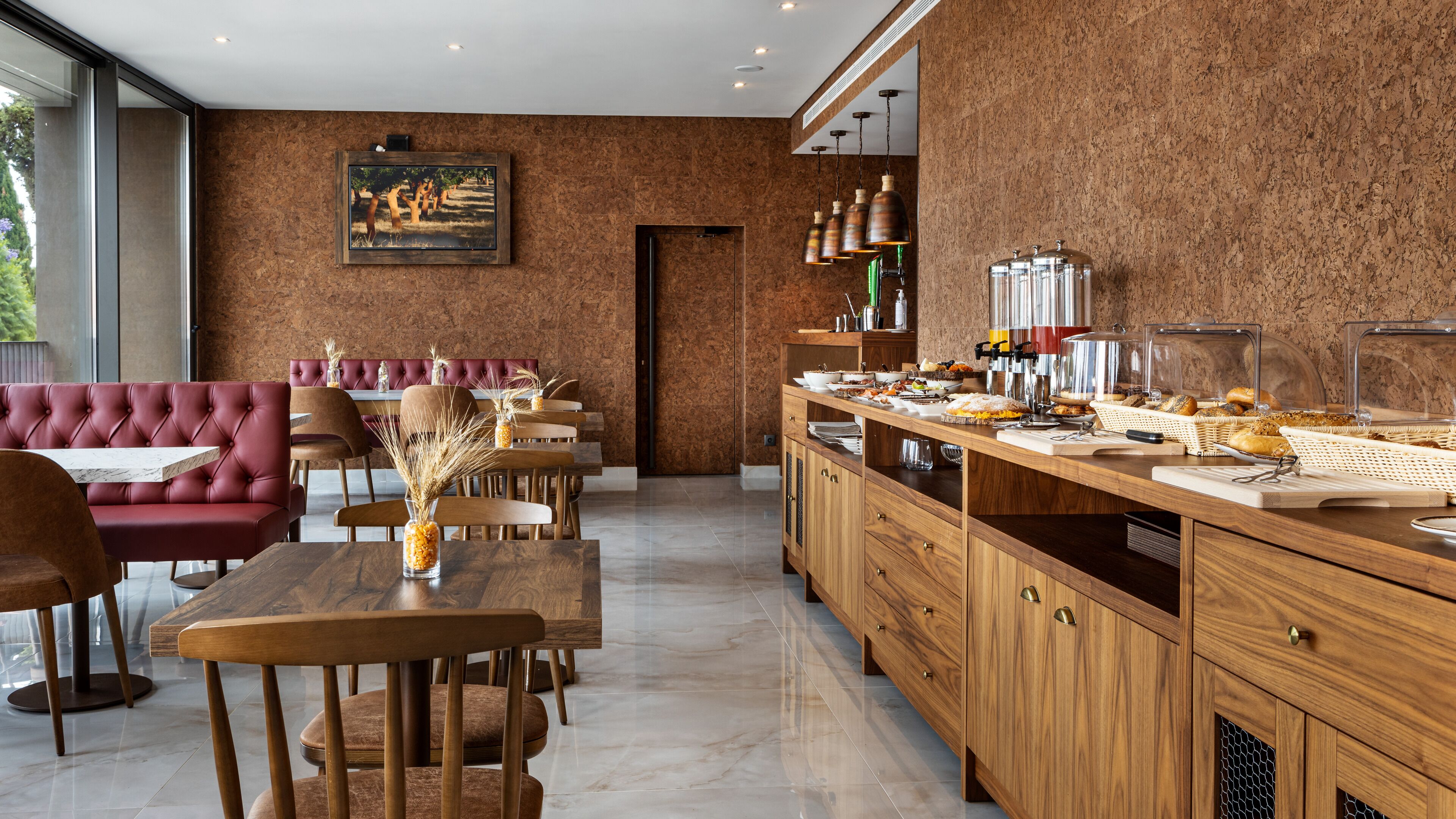 A modern dining area with a red upholstered bench, wooden tables, and chairs. A buffet counter with various food items is visible.