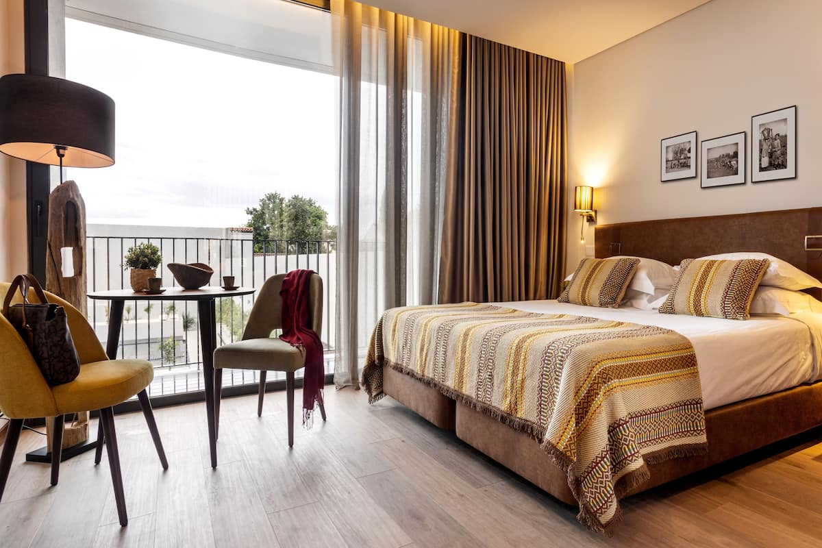 A hotel room with a large bed, a balcony with a table and chairs, and a view of the city.