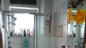 Ein Badezimmer mit Toilette, Waschbecken und Dusche. Auf dem Waschbecken liegen Pflegeprodukte und ein Handtuch hängt an der Wand.