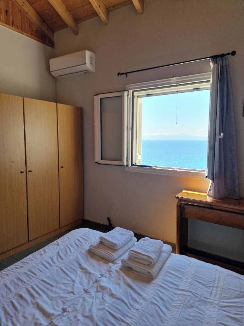 A bedroom with a bed, a wardrobe, a window with a view, and an air conditioning unit.