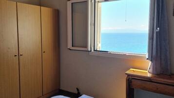 A bedroom with a bed, a wardrobe, a window with a view, and an air conditioning unit.