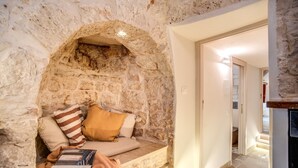 Una habitación acogedora con pared de piedra, un banco acolchado y una puerta que da a otra zona.