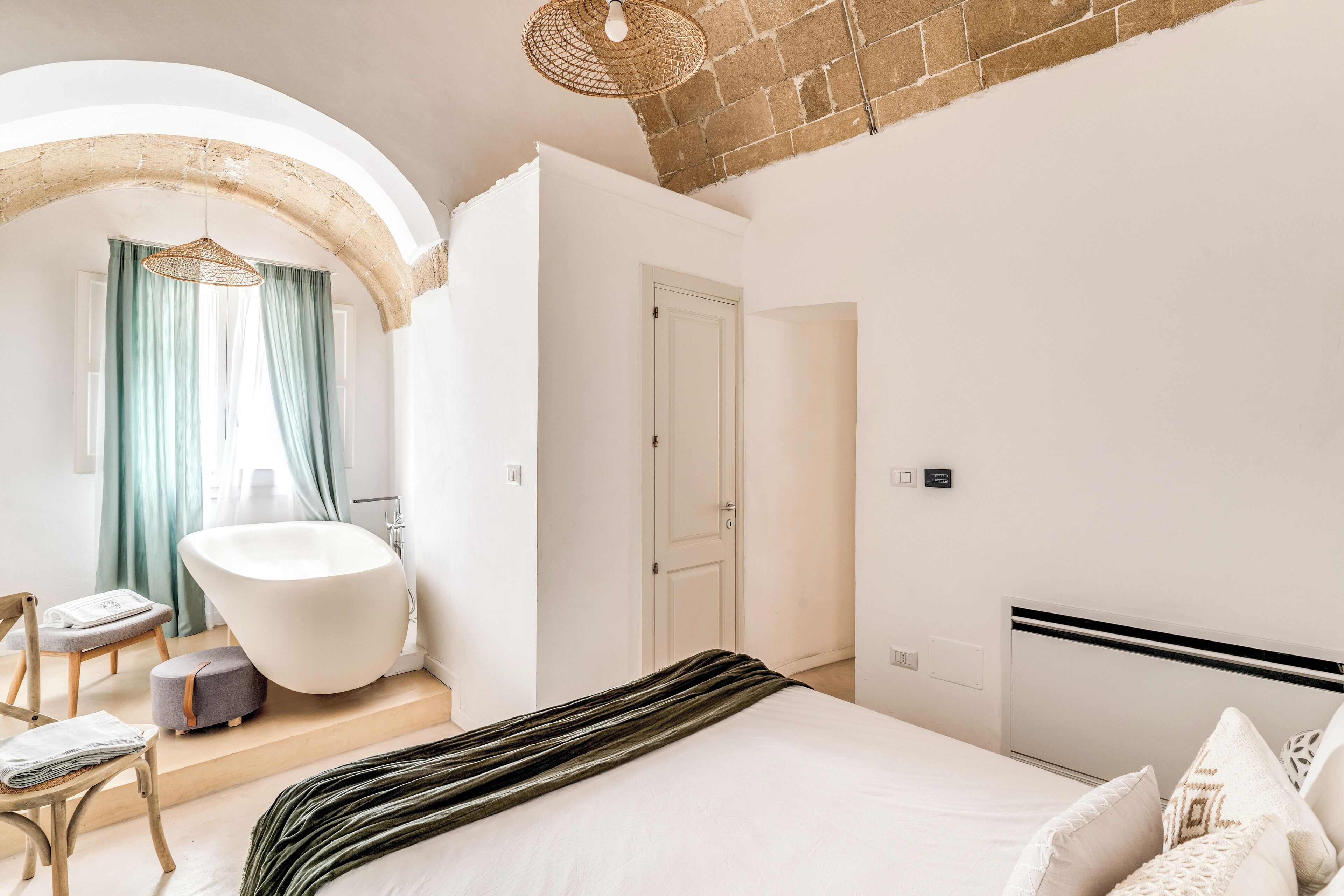 Ein modernes Schlafzimmer mit einem großen Bett, einer freistehenden Badewanne und einer kleinen Sitzecke.