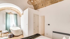A modern bedroom with a large bed, a freestanding bathtub, and a small seating area.