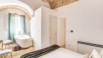 Ein modernes Schlafzimmer mit einem großen Bett, einer freistehenden Badewanne und einer kleinen Sitzecke.